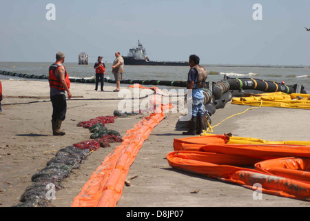 Les gens sont vus sur une plage utilisant des barrages résistants au pétrole pour contenir ou nettoyer les déversements de pétrole dans l'eau. Ces barrières aident à prévenir la propagation des polluants et à protéger l'environnement. Banque D'Images