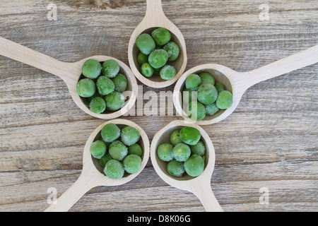 Pois verts congelés sur des cuillères en bois disposées en cercle Banque D'Images