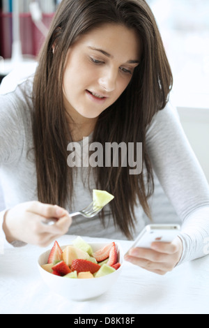 Portrait of a young woman eating fruit salad lors de la navigation avec son iphone Banque D'Images