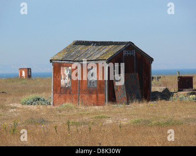 Cette photo montre une cabane rustique située dans la région de Dungeness, probablement près de la côte. L'image capture le bois altéré et la structure simple du bâtiment sur un fond naturel. Banque D'Images