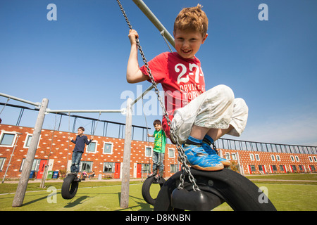 Les enfants jouent sur des balançoires en face de maisons à Almere avec panneaux solaires photovoltaïques sur le toit. Banque D'Images