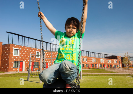 Les enfants jouent sur des balançoires en face de maisons à Almere avec panneaux solaires photovoltaïques sur le toit. Banque D'Images