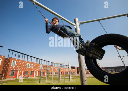 Les enfants jouent sur des balançoires en face de maisons à Almere avec panneaux solaires photovoltaïques sur le toit. Banque D'Images