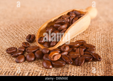 Les grains de café se répandre à partir d'un scoop sur un fond de jute ou de jute. Banque D'Images