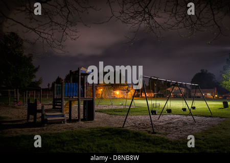 Une scène d'un effrayant désert aire de jeux pour enfants dans un parc de la banlieue de nuit. Banque D'Images