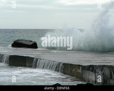 Les vagues s'écrasent contre une jetée, capturant l'énergie et le mouvement de l'océan. Cette image représente l'interaction entre la mer et les structures artificielles, avec des éclaboussures d'eau contre la jetée en bois ou en béton. Banque D'Images