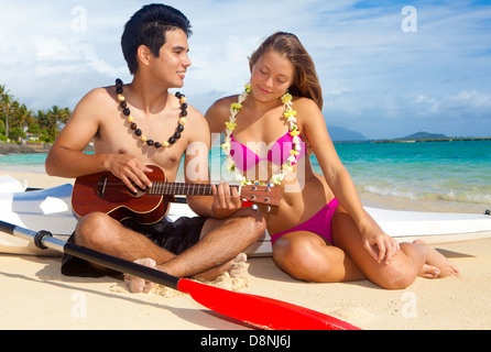 Couple sur la plage avec leurs skis surf jouer ukulele Banque D'Images