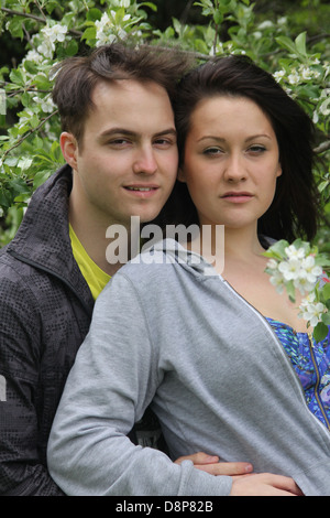 Cute young couple standing proche ensemble il a derrière elle, il à par-dessus son épaule, parmi les fleurs de l'arbre blanc. Banque D'Images