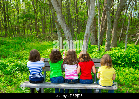 Enfants soeur et ami filles assis sur banc de parc à la forêt à vue arrière Banque D'Images