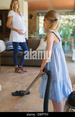 Petite fille à l'aspirateur, mère enceinte en arrière-plan Banque D'Images