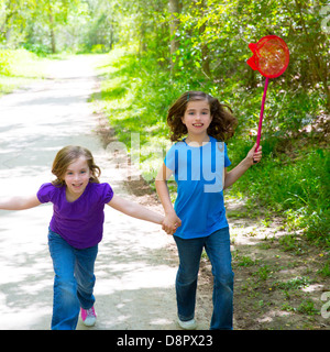 Les amis et ma soeur filles exécutant dans la piste en forêt smiling happy avec butterfly net Banque D'Images