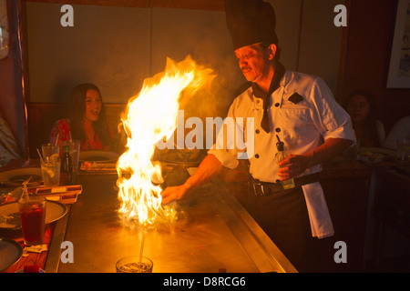 Un chef prépare un barbecue japonais sur une crêpière avec flammes jusqu'exciter les jeunes femmes. Banque D'Images