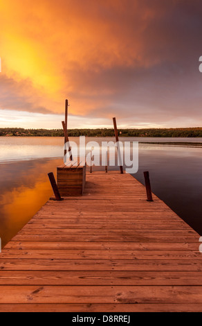 Vue le long d'une jetée en bois sur un lac au crépuscule, ciel bleu et orange vif, Suède Banque D'Images