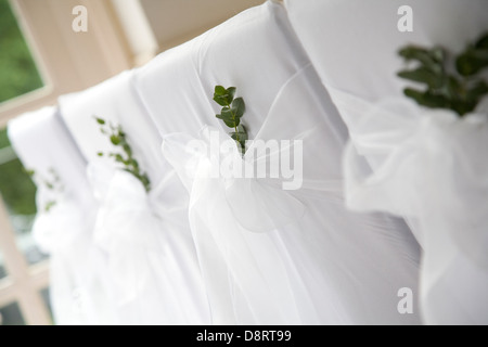 Dossiers de chaise couverts blanc organisé et décoré pour un mariage avec arcs et de mousseline de feuillage vert détail Banque D'Images