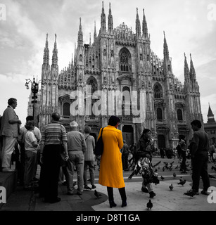 Une foule à l'extérieur de Duomo di Milano (la cathédrale de Milan), l'Italie, avec une femme dans un manteau jaune/orange standing out. Couleur sélective. Banque D'Images