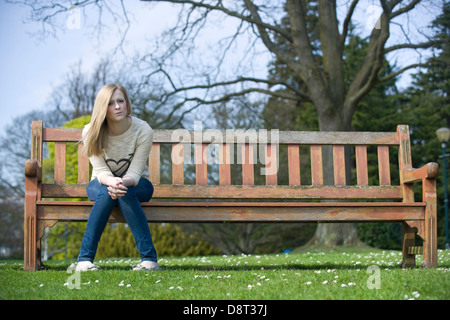 Une jeune femme assise sur un banc de parc par elle-même. Banque D'Images