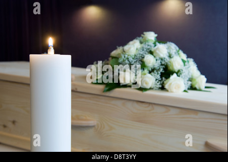 Une bougie brûlante avec un cercueil et un arrangement floral sur l'arrière-plan dans une morgue Banque D'Images