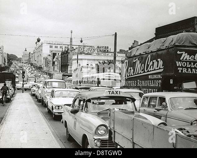Cette photographie de 1962 capture les embouteillages sur Parramatta Road à Sydney, mettant en évidence la nature animée de la vie urbaine et la présence de divers véhicules, y compris des taxis et des bus, dans un paysage urbain historique. Banque D'Images