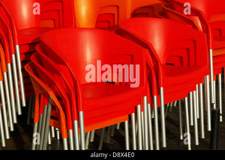 Gros plan sur une pile de chaises en plastique rouge qui brille sous les rayons du soleil Banque D'Images