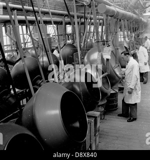 1950 historique. L'Angleterre. Les travailleurs d'usine mâle à revêtement blanc inspecter les matières fournitures médicales dans de grands fûts en acier. Banque D'Images