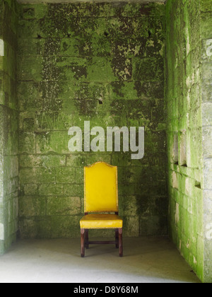 Un jaune vif chaise contre un mur couvert de lichens. Banque D'Images