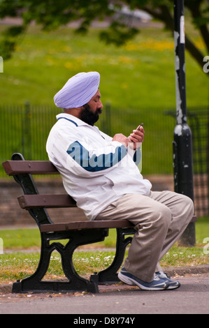 Homme Sikh assis dehors sur un banc portant un turban Banque D'Images