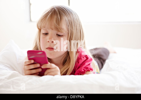 Girl lying on bed holding MP3 player Banque D'Images