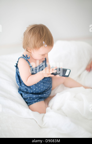 Little girl sitting on bed using cell phone Banque D'Images