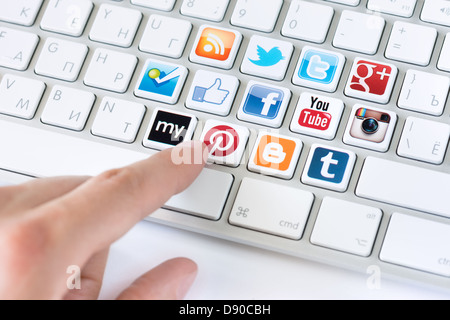 Main pointant sur le clavier avec les médias sociaux logotype collection de réseau social bien connu de la marque placée sur les touches du clavier Banque D'Images