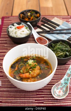 Soupe Asiatique aux crevettes dans white ceramic bowl composé avec cuillère en céramique avec sauce rouge épicée, asiatique de baguettes. Banque D'Images