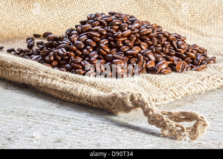 Sac de jute sur les grains de café - tas de grains de café torréfiés sur une toile ou un sac de jute. Banque D'Images