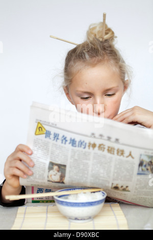 Girl with hair bun reading newspaper Banque D'Images