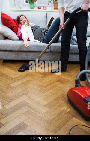 Une femme enceinte allongée sur un divan et un homme à l'aspirateur, la Suède. Banque D'Images