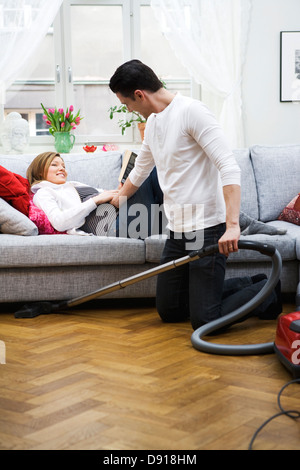 Une femme enceinte allongée sur un divan et un homme à l'aspirateur, la Suède. Banque D'Images