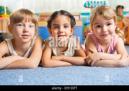 Trois belles filles se trouvant sur le plancher à la garderie Banque D'Images
