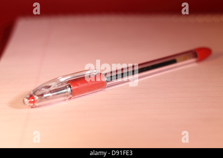 Stylo rouge sur le bloc-notes de rose clair. Banque D'Images