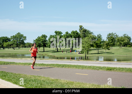 Un Caucasian woman jogging sur les sentiers alors que 4 hommes jouer au golf dans la distance au lac Hefner, Oklahoma City, Oklahoma, USA. Banque D'Images