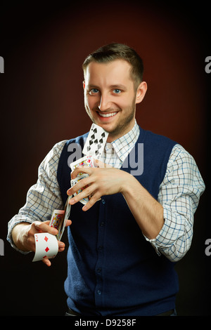 Heureux homme habile magicien cartes à jouer la scène jongleries en regardant la caméra sur fond sombre. Banque D'Images