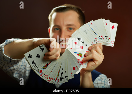 Heureux homme habile magicien cartes à jouer la scène jongleries sur fond sombre. Selective focus sur des cartes. Banque D'Images