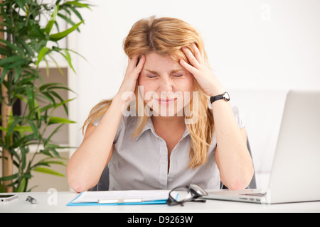 Femme mature avec maux de tête assis à la table dans le bureau Banque D'Images