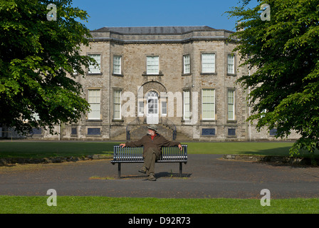 Homme senior assis sur le banc devant la Abbé Hall Art Gallery, Kendal, Cumbria, Angleterre Banque D'Images