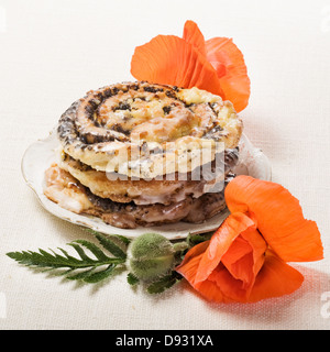 Petits pains aux graines de pavot, pâtisserie traditionnelle allemande Mohnschnecke, sur la plaque avec des fleurs de pavot Banque D'Images