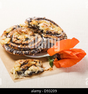 Petits pains aux graines de pavot, pâtisserie traditionnelle allemande Mohnschnecke, sur du papier sulfurisé avec fleur de pavot Banque D'Images