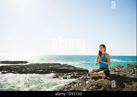 Mixed Race woman meditating on Rocky beach Banque D'Images