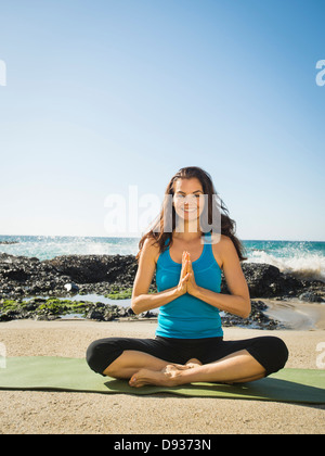 Mixed Race woman meditating on beach Banque D'Images