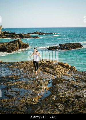 Mixed Race woman running on Rocky beach Banque D'Images