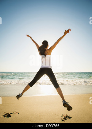 Mixed Race woman jumping for joy on beach Banque D'Images