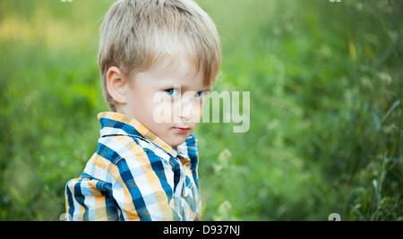 Un mignon petit garçon dans un champ d'herbe verte dans le parc Banque D'Images