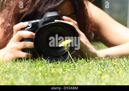 Gros plan d'une jolie fille de prendre une photo d'une fleur sur l'herbe dans un parc Banque D'Images