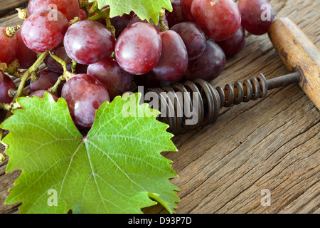 Ancien tire-bouchon est entre les feuilles de vigne et raisins rouges sur fond de bois rustique Banque D'Images